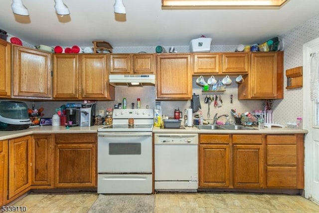 kitchen featuring brown cabinets, a sink, white appliances, under cabinet range hood, and wallpapered walls