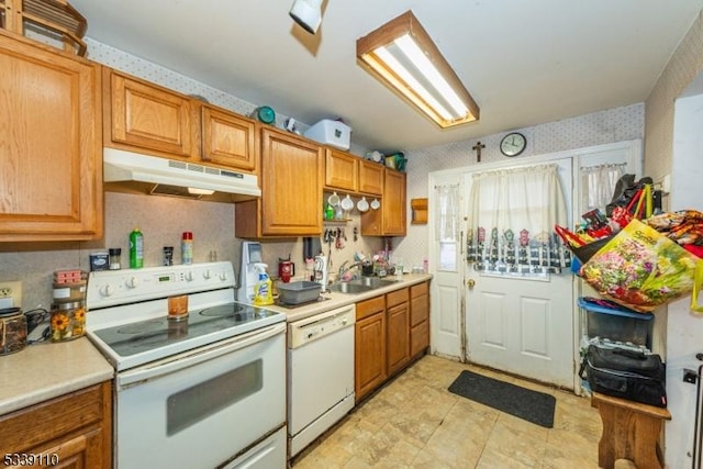 kitchen featuring light countertops, a sink, white appliances, under cabinet range hood, and wallpapered walls