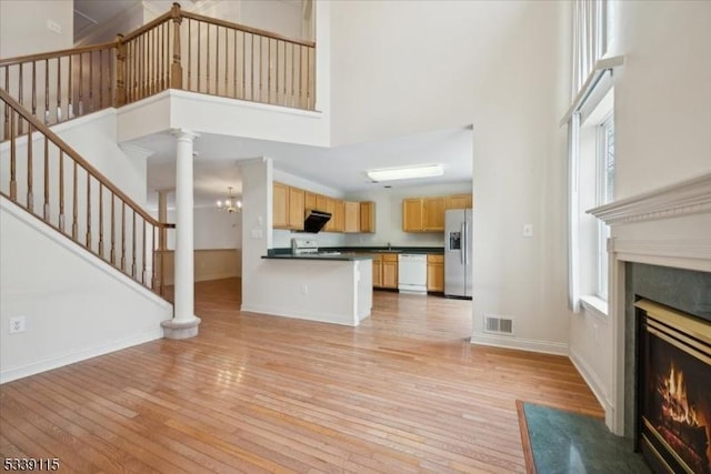 unfurnished living room with light wood finished floors, a towering ceiling, stairway, a fireplace with flush hearth, and baseboards