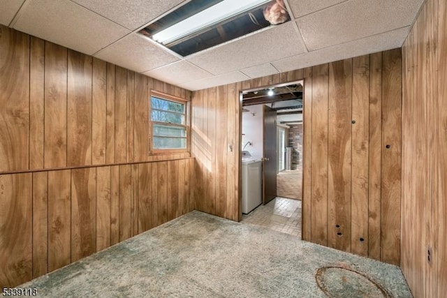 unfurnished room featuring wood walls, washer / clothes dryer, a drop ceiling, and light colored carpet