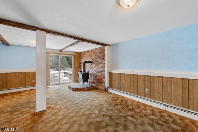 unfurnished living room featuring a wainscoted wall, a wood stove, baseboard heating, wood walls, and beam ceiling