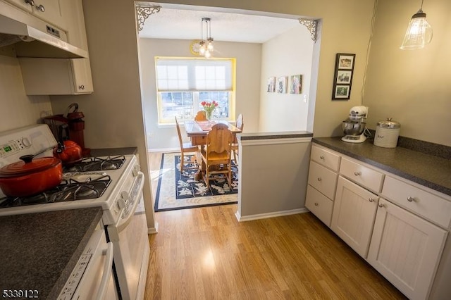 kitchen featuring under cabinet range hood, white gas range, light wood finished floors, dark countertops, and pendant lighting