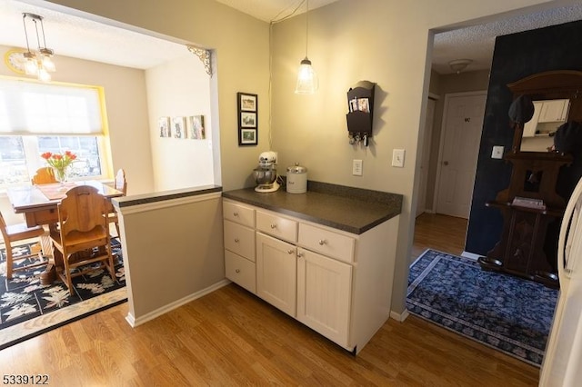 kitchen featuring dark countertops, pendant lighting, white cabinets, and light wood-style flooring