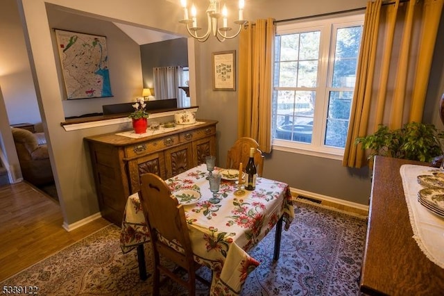 dining room with baseboards, wood finished floors, visible vents, and a notable chandelier