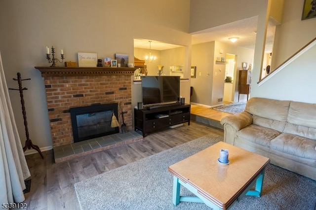 living area with a brick fireplace, baseboards, an inviting chandelier, and wood finished floors