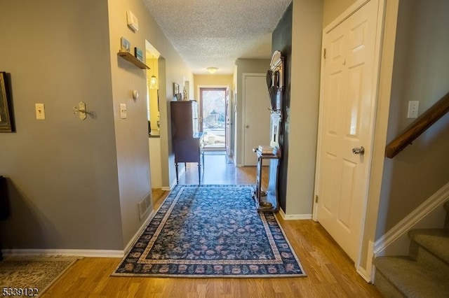 hallway with a textured ceiling, wood finished floors, visible vents, baseboards, and stairway