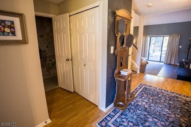 corridor with stairs, a textured ceiling, baseboards, and wood finished floors