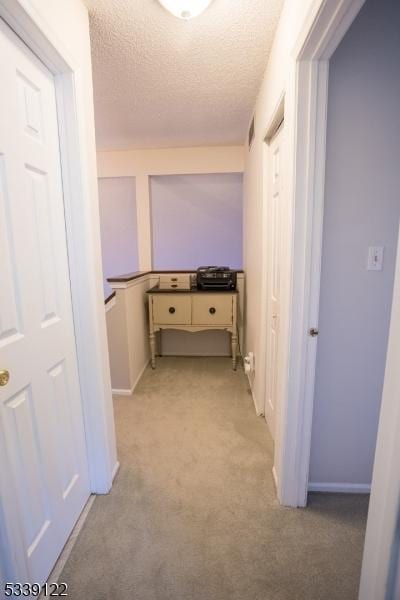 hallway with visible vents, light carpet, and a textured ceiling