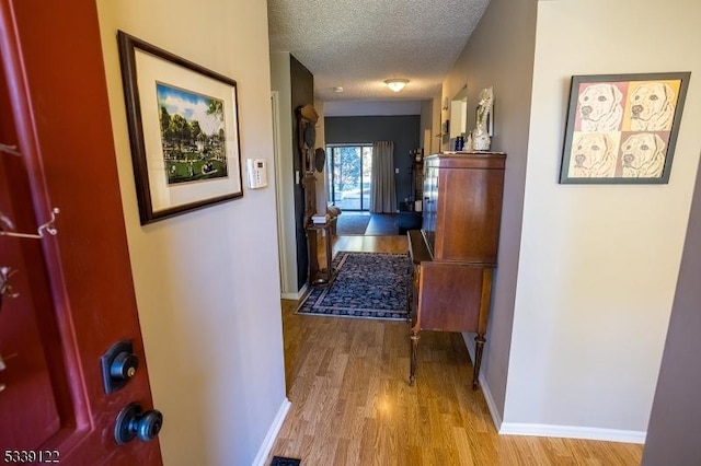 hallway featuring baseboards, a textured ceiling, and wood finished floors