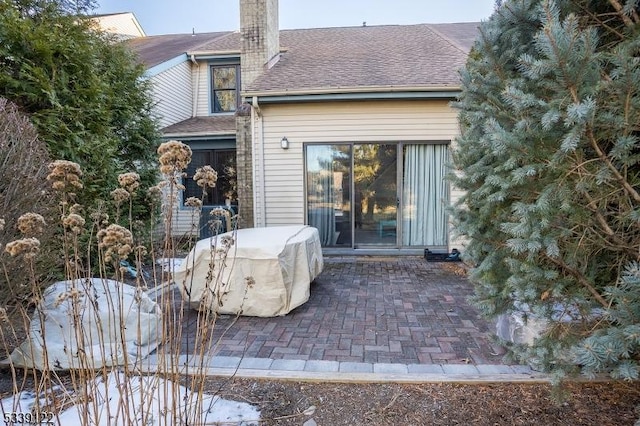 rear view of house featuring a patio, a chimney, and roof with shingles