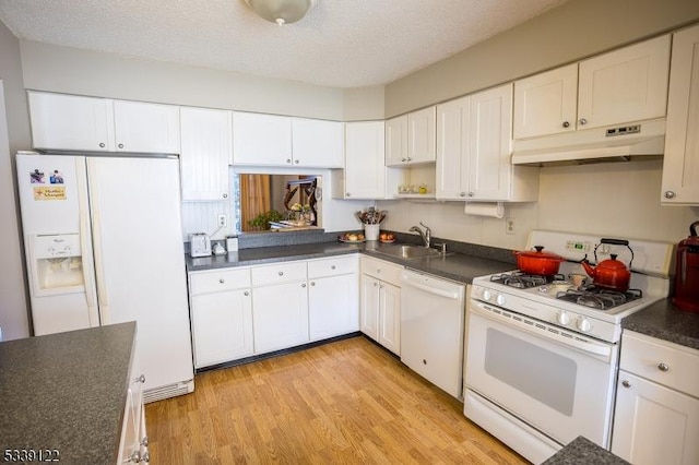 kitchen featuring white appliances, light wood finished floors, dark countertops, under cabinet range hood, and a sink