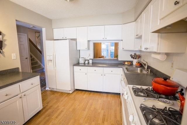 kitchen with dark countertops, white cabinets, a sink, light wood-type flooring, and white appliances