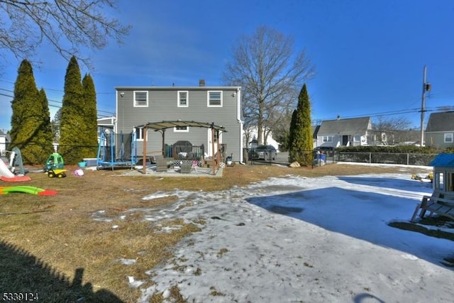 snow covered rear of property with a trampoline and a pergola