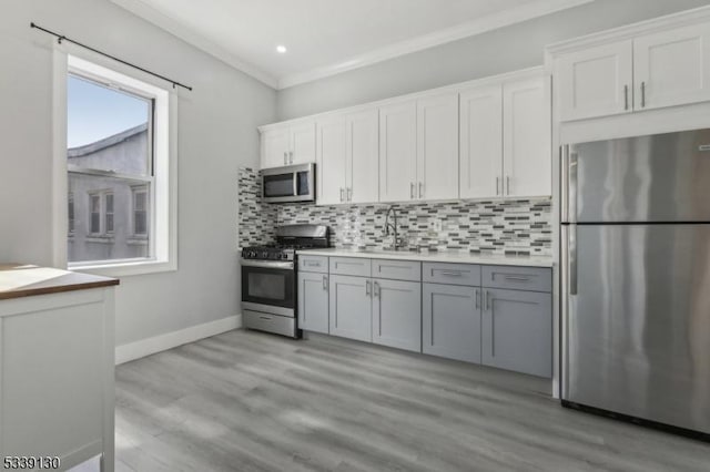 kitchen featuring light wood finished floors, stainless steel appliances, tasteful backsplash, ornamental molding, and a sink