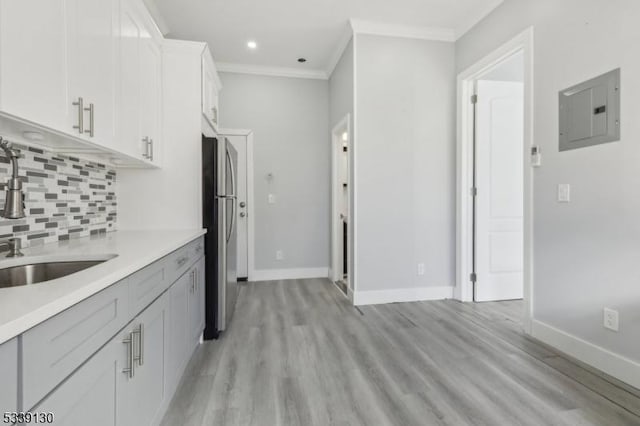 kitchen with a sink, ornamental molding, decorative backsplash, freestanding refrigerator, and electric panel