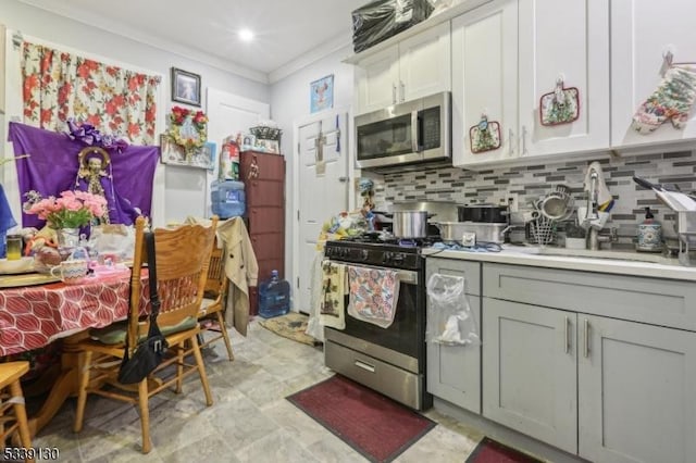 kitchen with tasteful backsplash, appliances with stainless steel finishes, light countertops, crown molding, and a sink