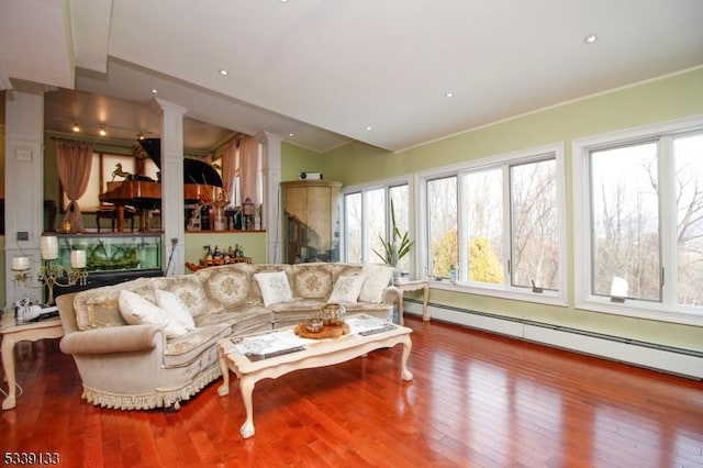 living area with vaulted ceiling, baseboard heating, wood finished floors, and ornate columns