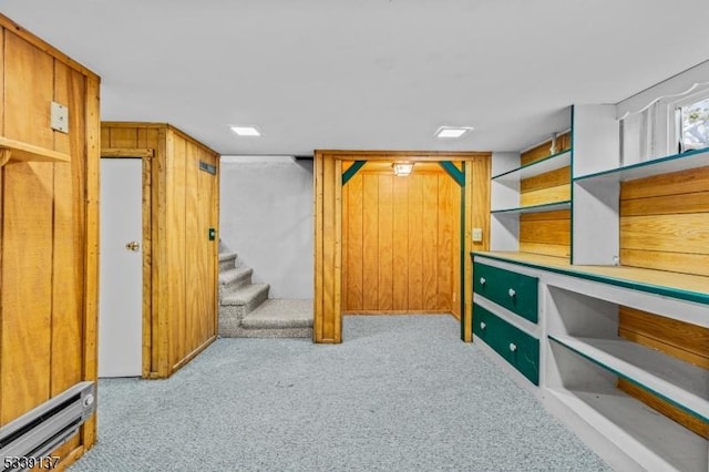 finished basement featuring light carpet, wooden walls, stairs, and a baseboard heating unit