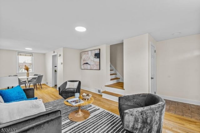 living room featuring light wood finished floors, stairway, visible vents, and baseboards