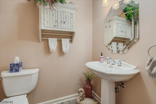 half bathroom featuring toilet, baseboards, and a sink