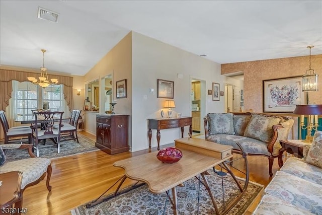 living area featuring a chandelier, visible vents, light wood-style floors, and vaulted ceiling