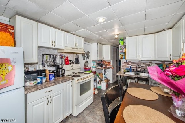 kitchen featuring a paneled ceiling, under cabinet range hood, white appliances, white cabinets, and tile patterned floors