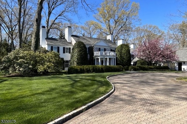 view of front facade featuring decorative driveway, a chimney, a front yard, and a balcony