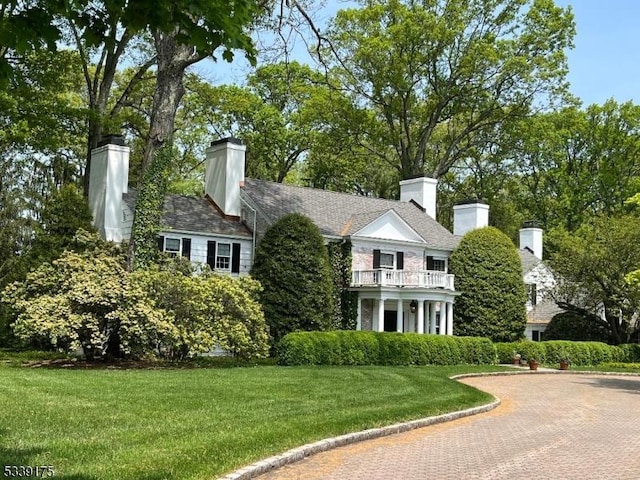 view of front of property with a chimney, a balcony, and a front lawn