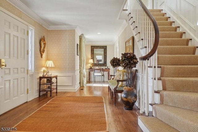 entrance foyer featuring ornamental molding, stairs, a decorative wall, and wood finished floors