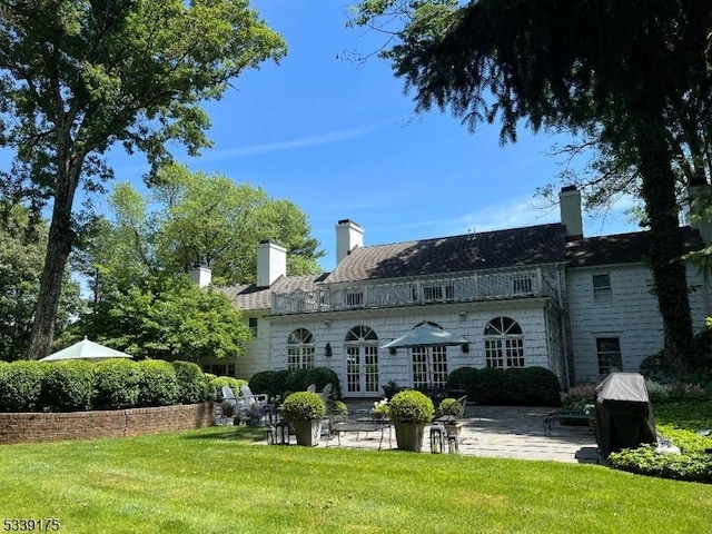 rear view of house featuring a patio area, a chimney, a lawn, and french doors