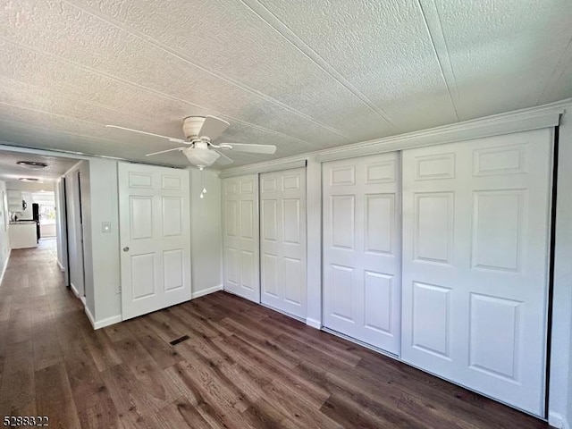 unfurnished bedroom featuring ceiling fan, dark wood-type flooring, a textured ceiling, and multiple closets