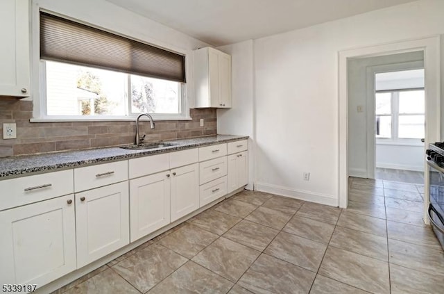 kitchen with decorative backsplash, white cabinetry, a sink, dark stone countertops, and baseboards