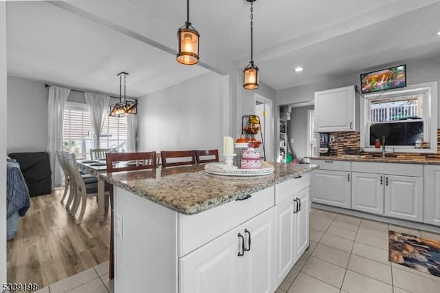 kitchen featuring a center island, white cabinetry, hanging light fixtures, and a sink