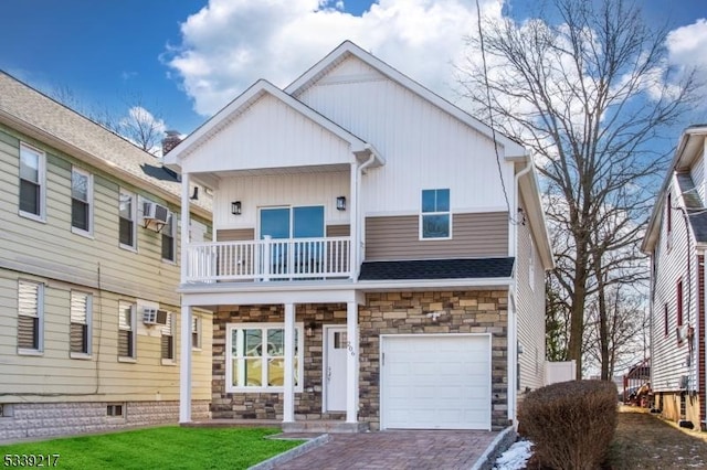 view of front of house featuring decorative driveway, an attached garage, board and batten siding, a balcony, and stone siding