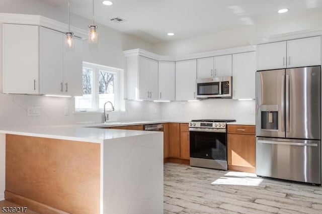 kitchen featuring decorative light fixtures, brown cabinets, backsplash, appliances with stainless steel finishes, and white cabinets