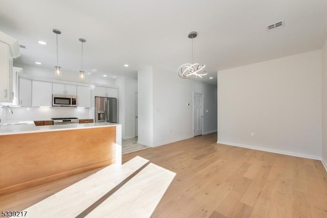 kitchen featuring visible vents, white cabinets, stainless steel appliances, light countertops, and pendant lighting