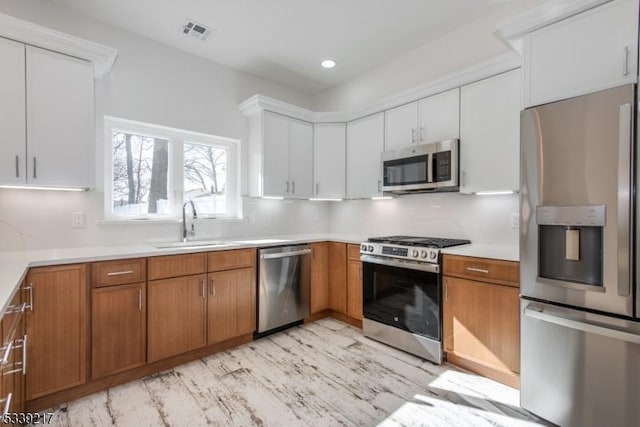 kitchen featuring light countertops, appliances with stainless steel finishes, brown cabinetry, and white cabinets