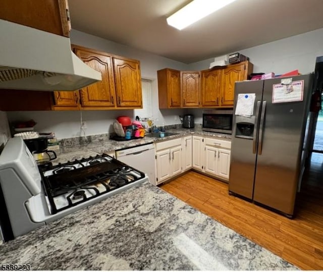 kitchen featuring appliances with stainless steel finishes, light hardwood / wood-style floors, light stone countertops, and extractor fan