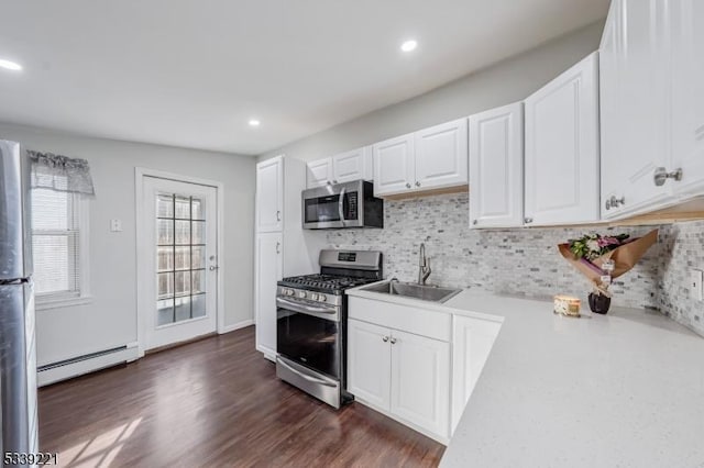 kitchen with light countertops, appliances with stainless steel finishes, a baseboard heating unit, white cabinets, and a sink