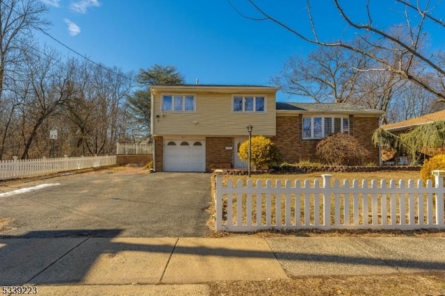 view of front of house featuring driveway, brick siding, a fenced front yard, and an attached garage