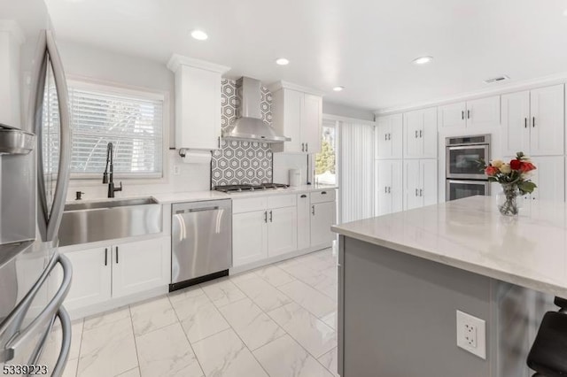 kitchen with marble finish floor, stainless steel appliances, white cabinets, a sink, and wall chimney exhaust hood