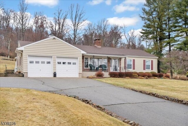 ranch-style home with driveway, an attached garage, covered porch, a chimney, and a front lawn