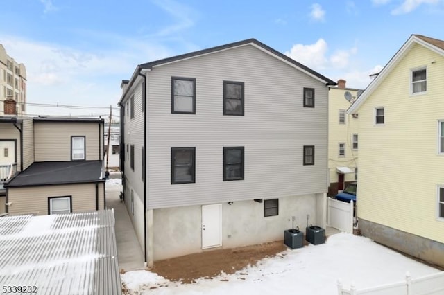 snow covered house featuring central AC unit and fence