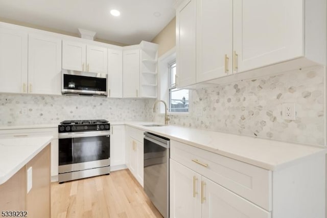 kitchen with open shelves, light stone counters, stainless steel appliances, white cabinetry, and a sink