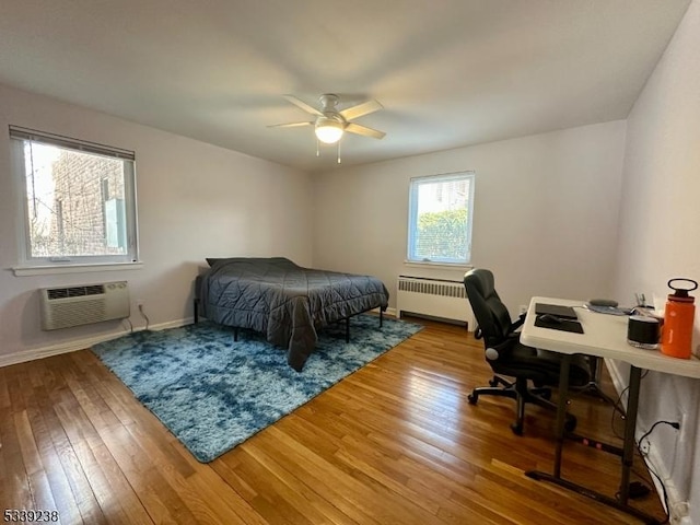 bedroom featuring light wood-type flooring, a wall mounted AC, radiator, and ceiling fan