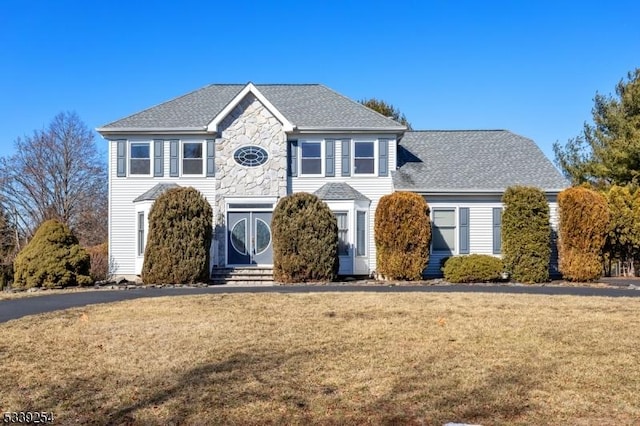 colonial home featuring entry steps, stone siding, a front lawn, and a shingled roof