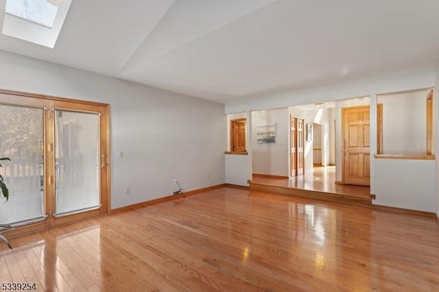 empty room with lofted ceiling with skylight, baseboards, and wood finished floors