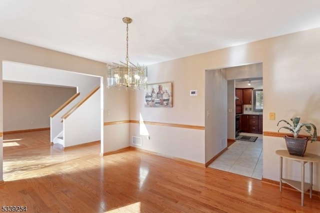 unfurnished dining area featuring baseboards, light wood-type flooring, visible vents, and a notable chandelier