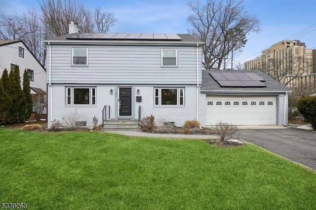 colonial home featuring an attached garage, a front lawn, aphalt driveway, and solar panels