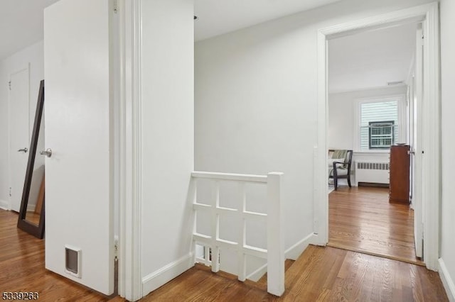 hallway featuring radiator heating unit, wood finished floors, an upstairs landing, and baseboards